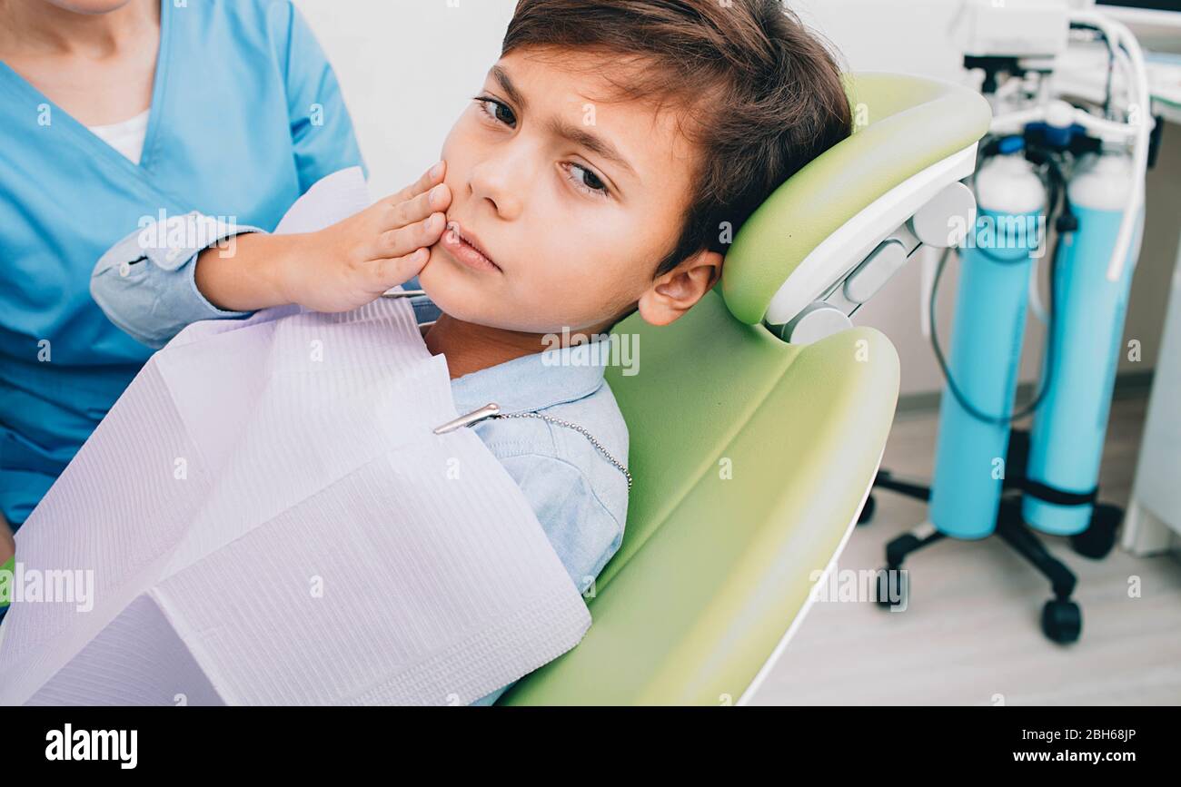 Kleiner Junge mit Zahnschmerzen sitzen auf Zahnstuhl. Zahnschmerzen, Kind traurig Blick auf die Kamera Stockfoto