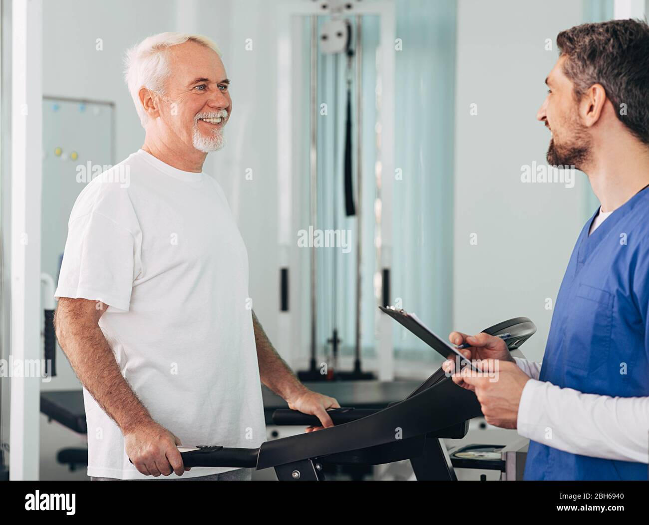 Leitender Patient, der mit seinem Therapeuten im Krankenhaus eine Physiotherapie durchgeführt hat. Ältere Mann Training auf dem Laufband. Stockfoto