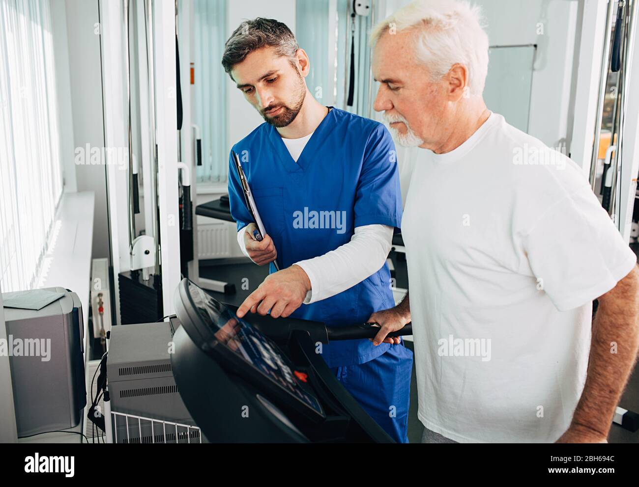 Leitender Patient, der mit seinem Therapeuten im Krankenhaus eine Physiotherapie durchgeführt hat. Ältere Mann Training auf dem Laufband. Stockfoto
