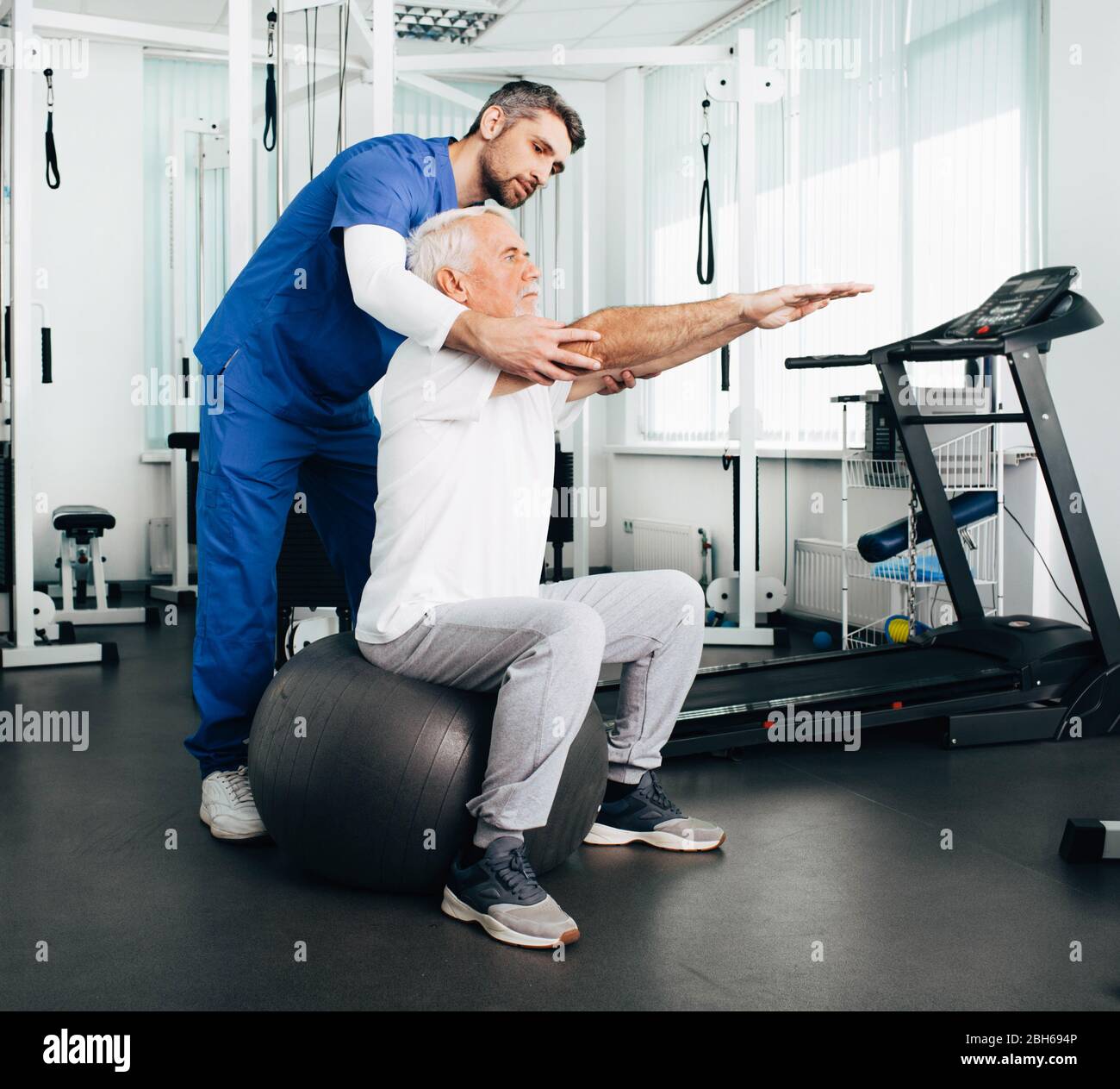 Senior Patient mit Physiotherapie Termin mit seinem Arzt. Mann tut nach der Rehabilitation Übung, während auf einem Fitness-Ball sitzen. Stockfoto