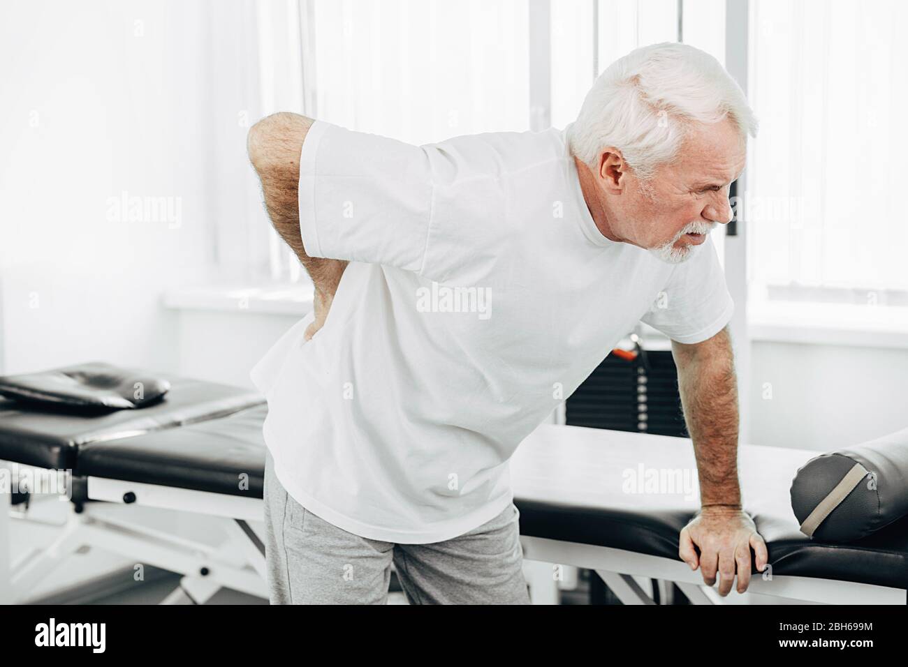 Älterer Mann, der unter Rückenschmerzen leidet. Stehen Sie im medizinischen Zentrum und fühlen sich schlecht Stockfoto