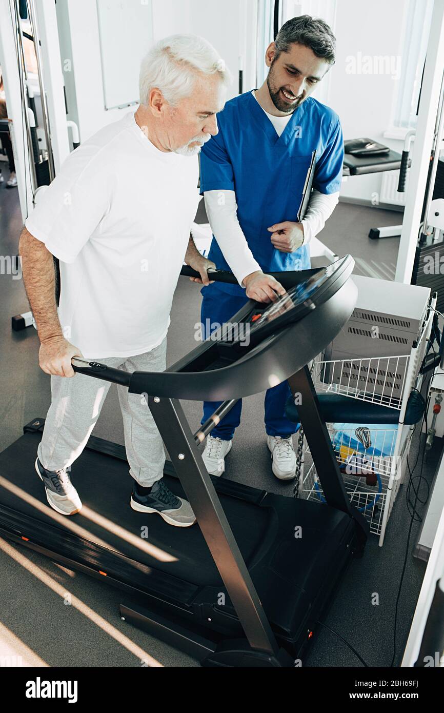 Älterer Mann, der Cardio-Training auf dem Laufband macht, hilft Therapeut älteren Patienten zur Erholung Stockfoto