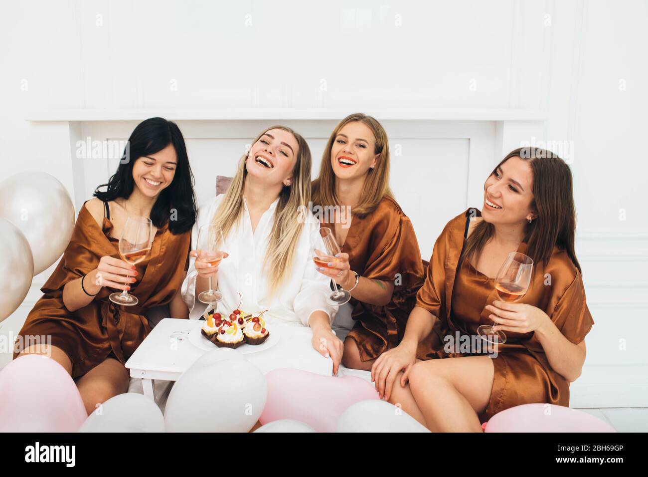 Schlafanzug Party time. Schöne charmante Freundinnen feiern Junggesellinnenabschied, trinken Alkohol und lachen im Hotel Stockfoto
