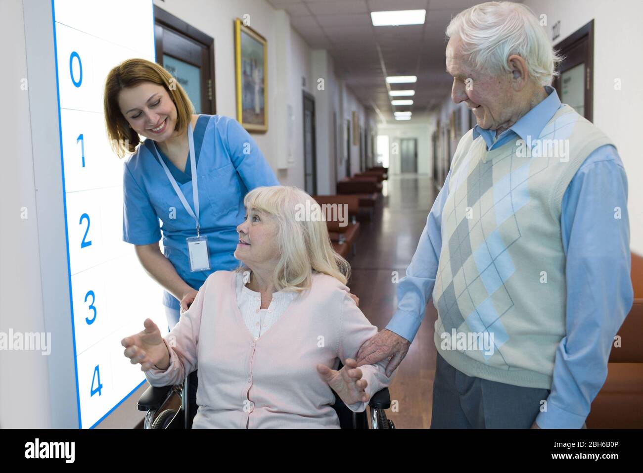 Ältere Frau im Rollstuhl im Gespräch mit der Krankenschwester in einem Krankenhaus hinter ihr standen älterer Mann. Stockfoto