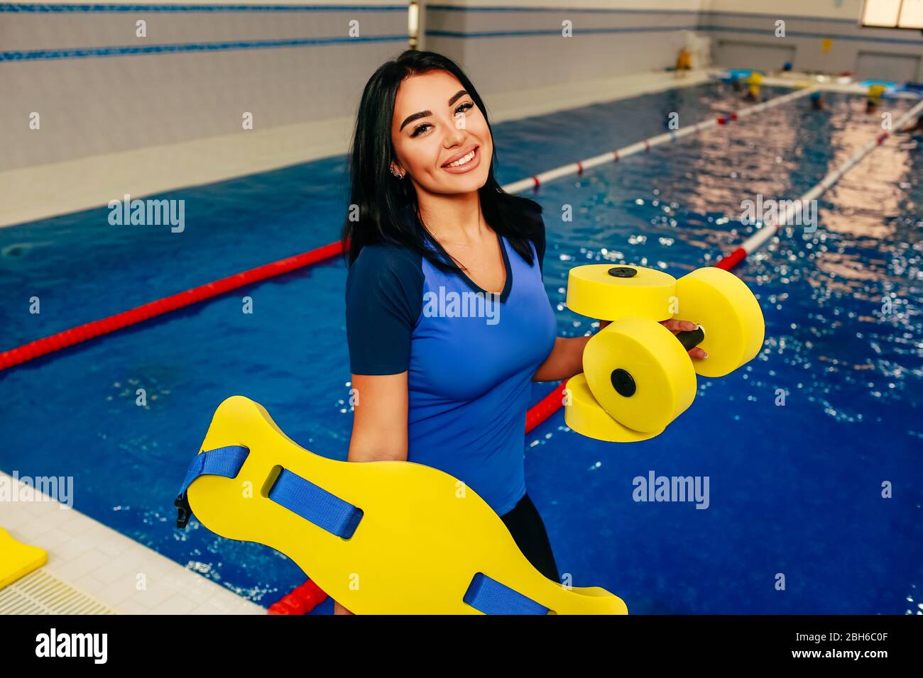 Sportliche Frau hält Fitness Barbells am Pool und sieht positiv in die Kamera. Aqua Fitness Instruktor Stockfoto