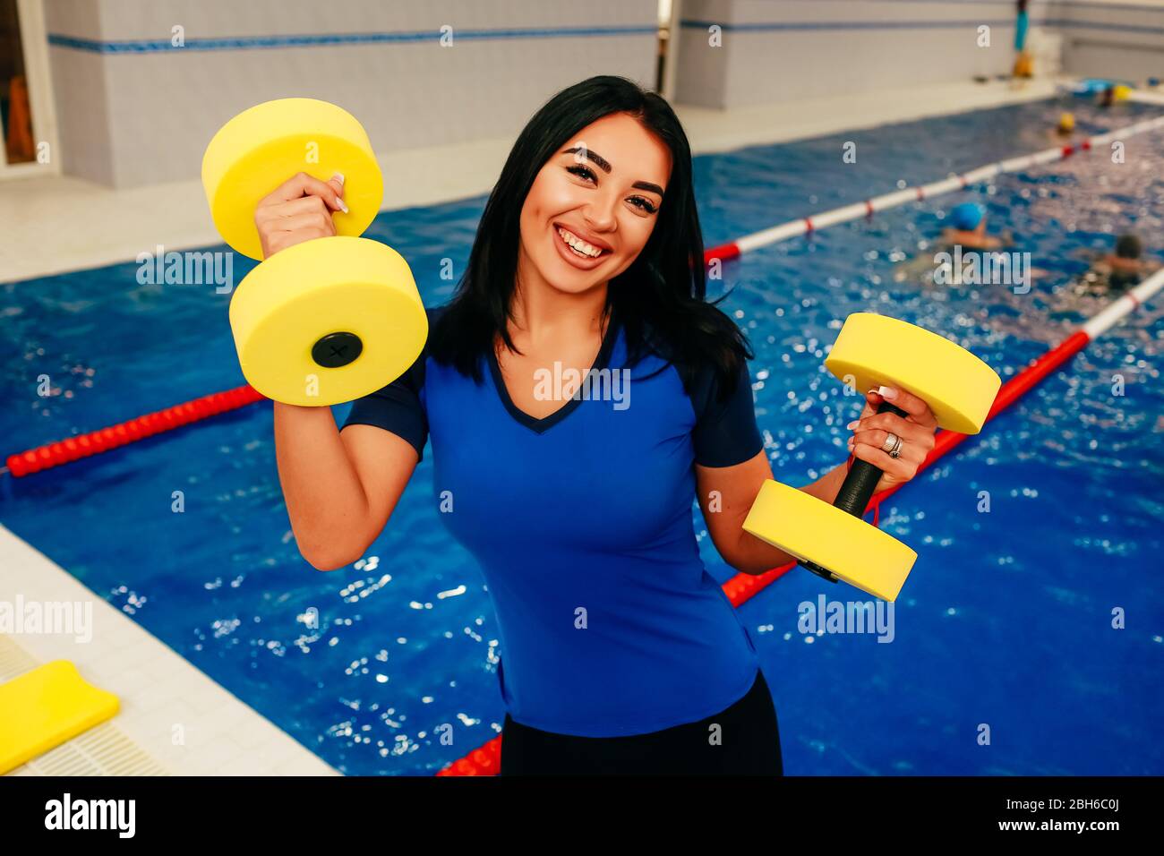 Sportliche Frau mit Schaumwasserhanteln am Pool und positivem Blick in die Kamera. Aqua-Aerobic-Trainer Stockfoto