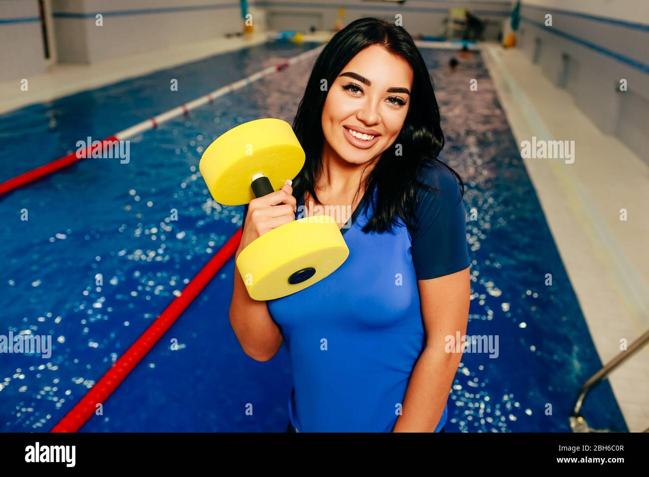 Sportliche Frau hält Aqua Aerobic-Zeug auf dem Hintergrund-Swimmingpool. Aqua-Fitnesstrainer Stockfoto