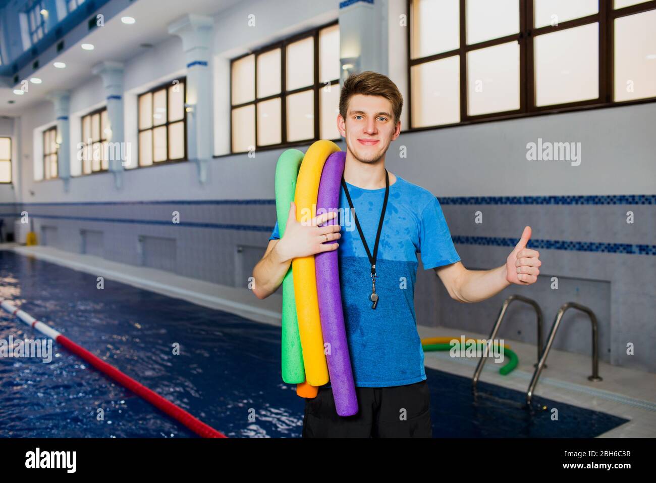 Fit lächelnden Mann hält Schaumstoffrolle und zeigt Daumen hoch Blick auf die Kamera am Schwimmbad. Portrait Schwimmlehrer Stockfoto