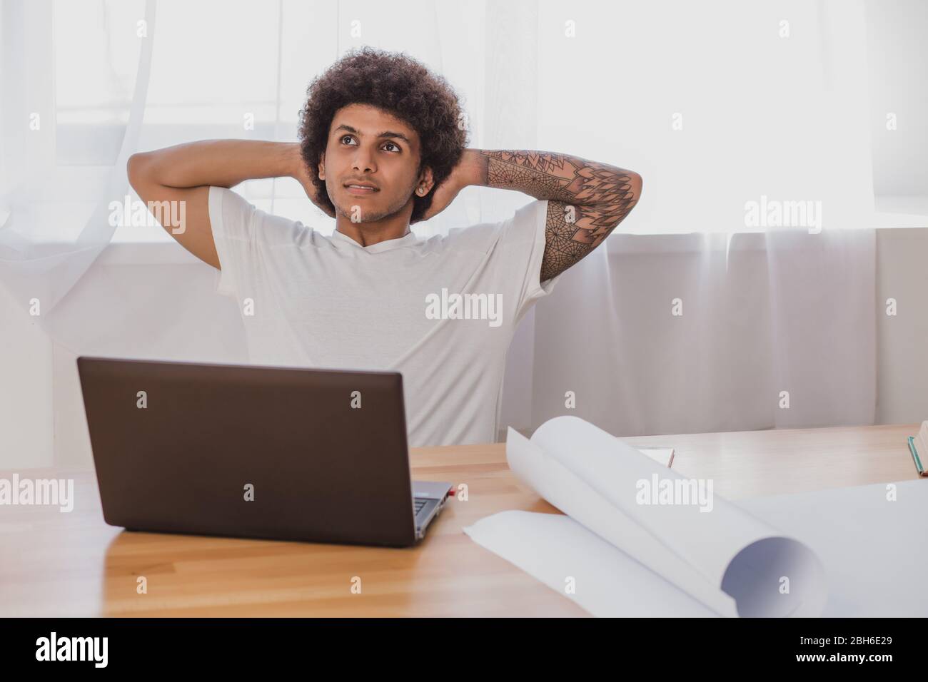 Lockiger Mann, der sich auf dem Stuhl zurücklehnt, während er an seinem Arbeitsplatz im Büro sitzt. Zeit entspannen, nach der Arbeit getan. Stockfoto