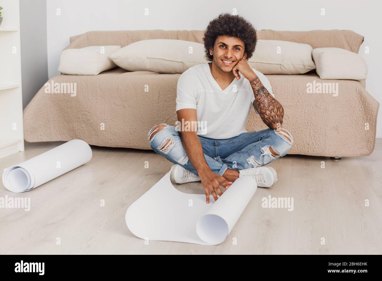 Positiv Lockenhaarige Mann öffnet ein leeres Blatt Papier für Zeichnungen, sitzen auf dem Boden zu Hause Stockfoto