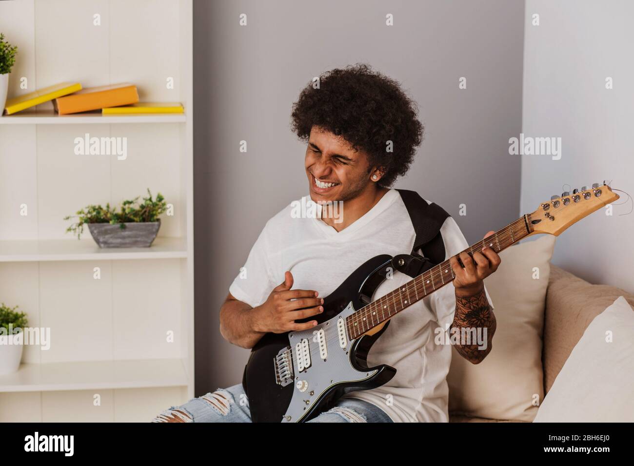 Musiker. Positiv Lockenhaariger Mann, ausdrucksstark spielt die Bassgitarre, zu Hause Stockfoto