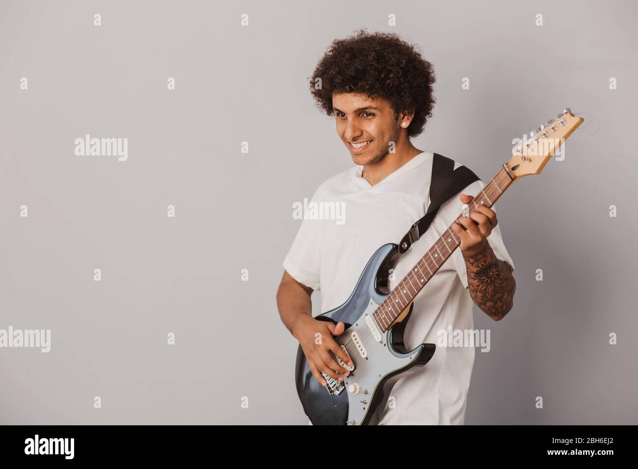 Positiv gelockte Mann, ausdrucksstark spielt die Bassgitarre, auf grauem Hintergrund. Fröhlicher Musiker. Stockfoto