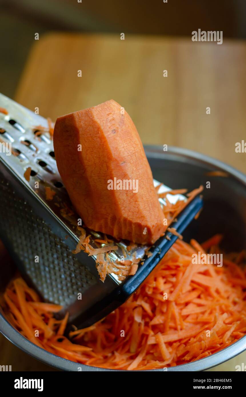 Ein großes Stück Karotten liegt auf einer Reibe. Unterbrochener Zerkleinerungsprozess rohes Gemüse. Der Prozess der Herstellung von Salat. Im echten Leben. Nahaufnahme. Selektiv fo Stockfoto