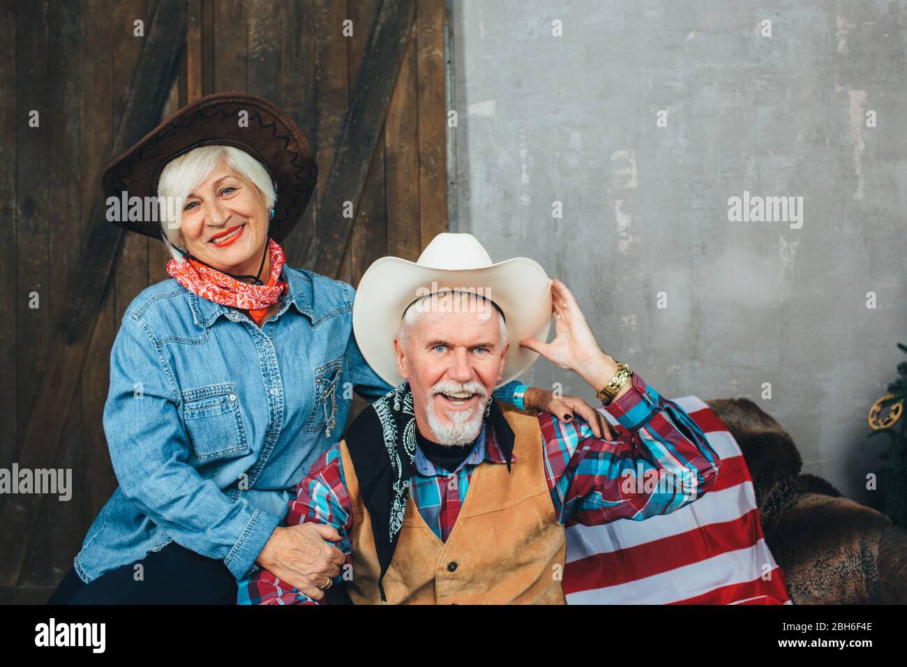 Ältere Paare im Cowboy-Stil, auf der Couch sitzend, einander anschauend. Stylische Senioren Stockfoto