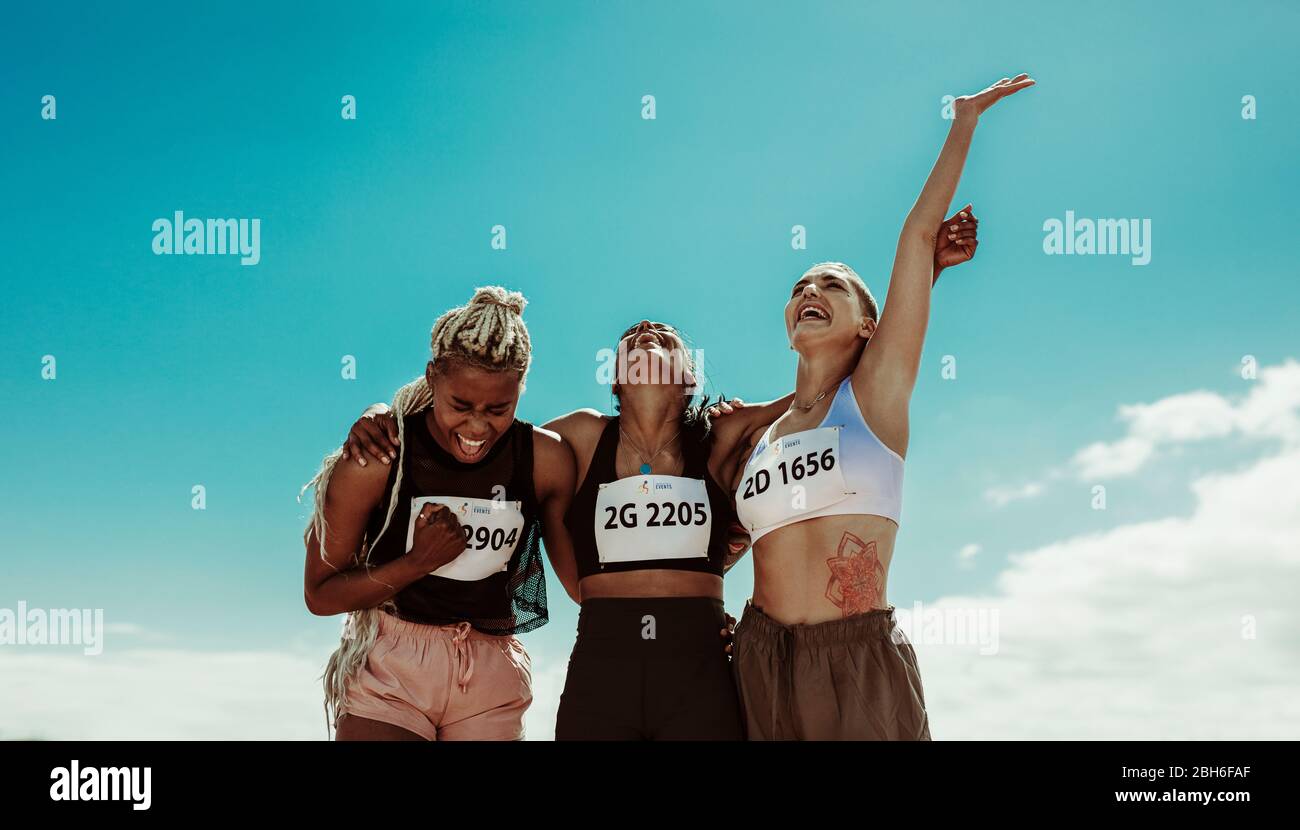 Gruppe von Athleten gegen Himmel. Drei junge Frauen schreien und freuen sich über den Sieg im Stadion. Stockfoto