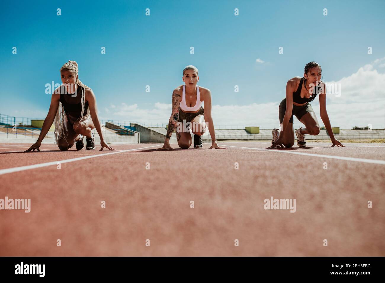 Drei Athletinnen bereiten sich auf Startblöcke im Stadion vor. Sprinter am Start Blöcke bereit für das Rennen. Stockfoto