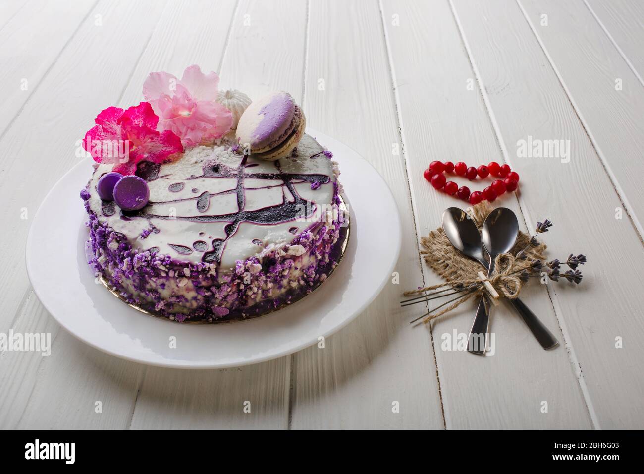 Hausgemachte Heidelbeer-Käsekuchen zum Valentinstag, mit Blumen und Makronen auf weißem Holztisch Hintergrund dekoriert. Draufsicht. Stockfoto
