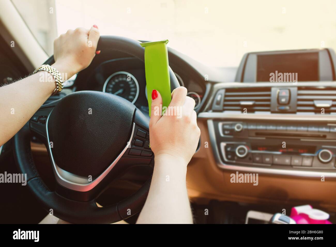Weibliche Hände halten einen Proteinriegel, während der Fahrt. Nicht im Fokus Armaturenbrett Auto. Gesunde und schnelle Lebensmittel während der Fahrt Stockfoto