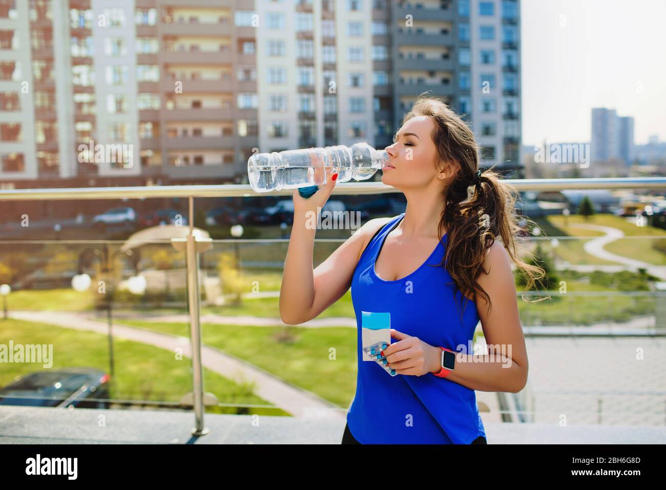 Sportliche Frau, die Wasser trinkt, entspannt, beim Workout im Freien. Sportler trinkt Pillen mit Wasser Stockfoto