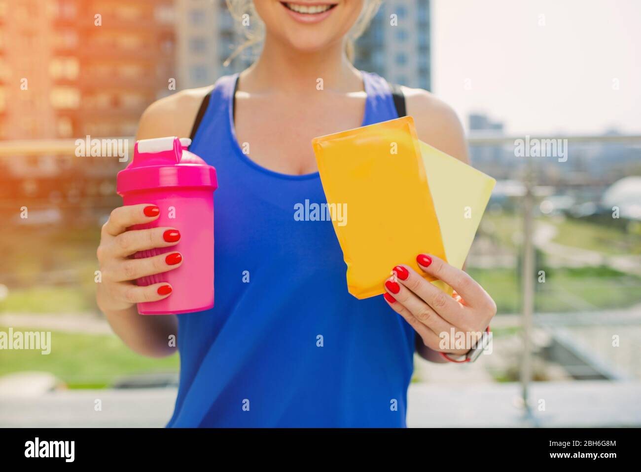 Eine sportliche Frau, die einen Shaker und Beutel mit einem löslichen Protein-Cocktail hält. Sporternährung für intensives Outdoor-Training. Stockfoto