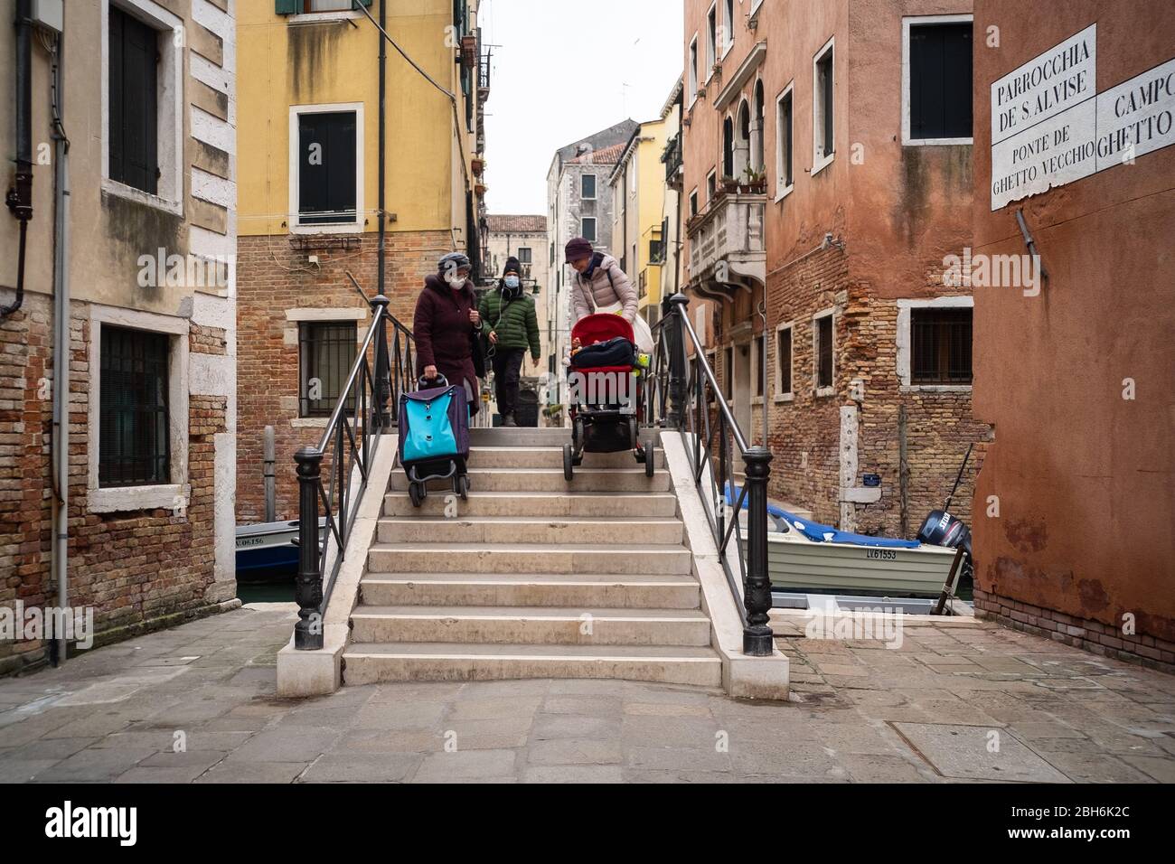 VENEDIG, ITALIEN - APRIL 2020: Menschen mit Schutzmasken überqueren eine Brücke im jüdischen Ghetto von Venedig während der nationalen Sperre für Covid-19 pande Stockfoto