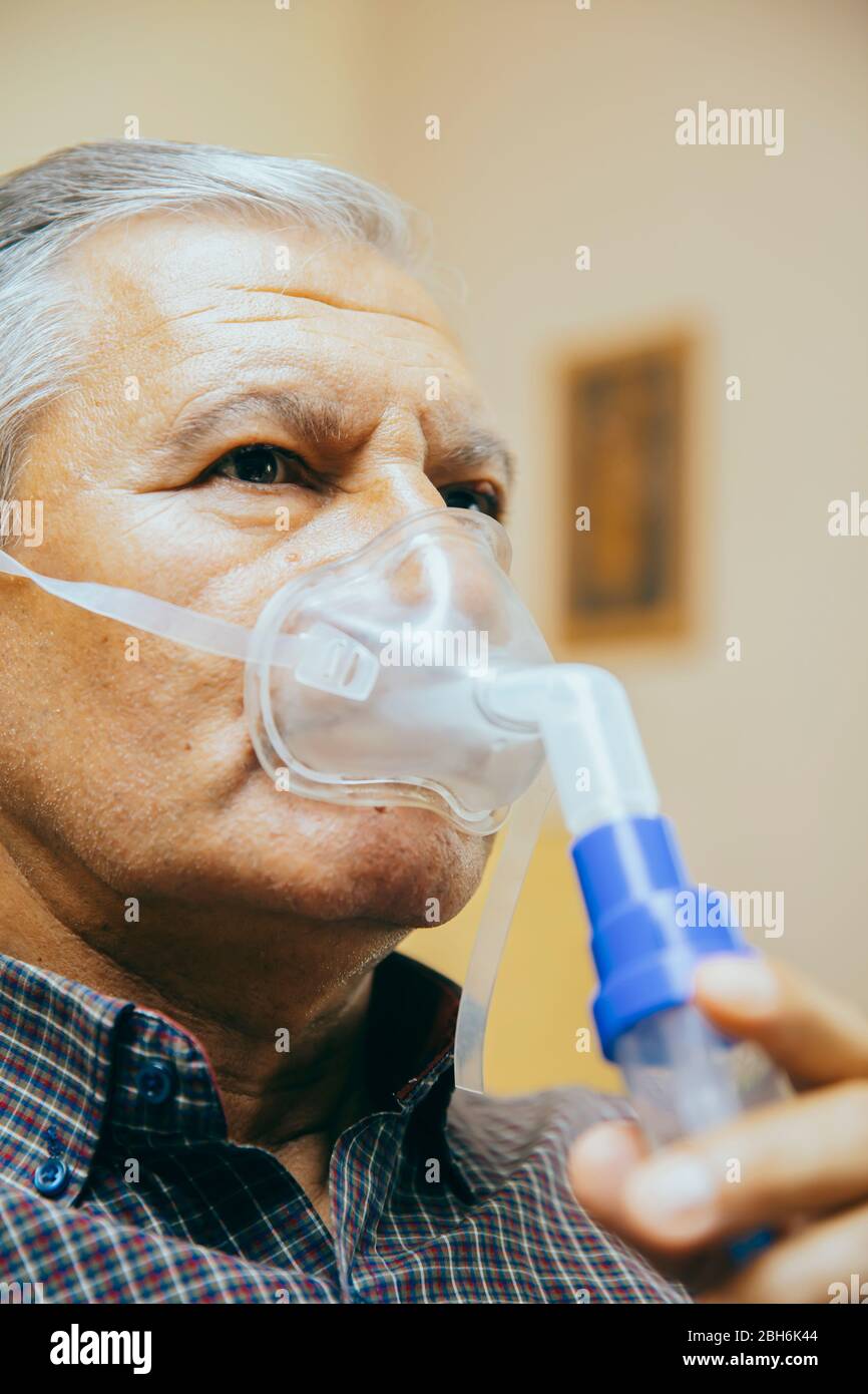 Leitender Mann, der medizinische Geräte für die Inhalation mit Atemschutzmaske verwendet, Vernebler im Zimmer Stockfoto