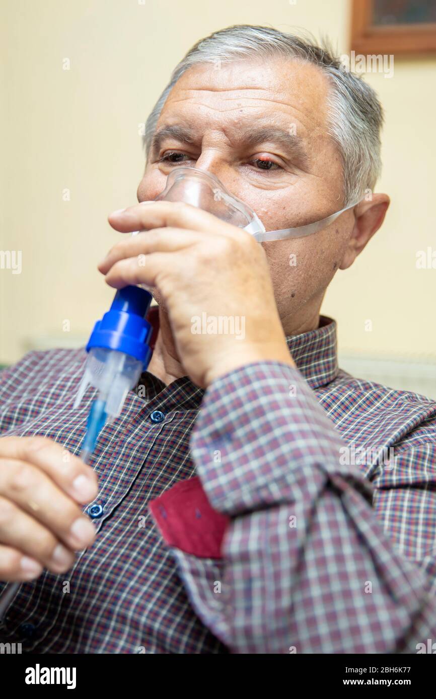 Leitender Mann, der medizinische Geräte für die Inhalation mit Atemschutzmaske verwendet, Vernebler im Zimmer Stockfoto