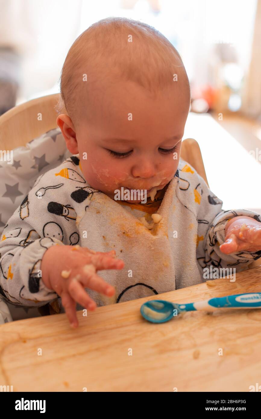 Niedliches Baby, das aus dem Hochstuhl isst Stockfoto