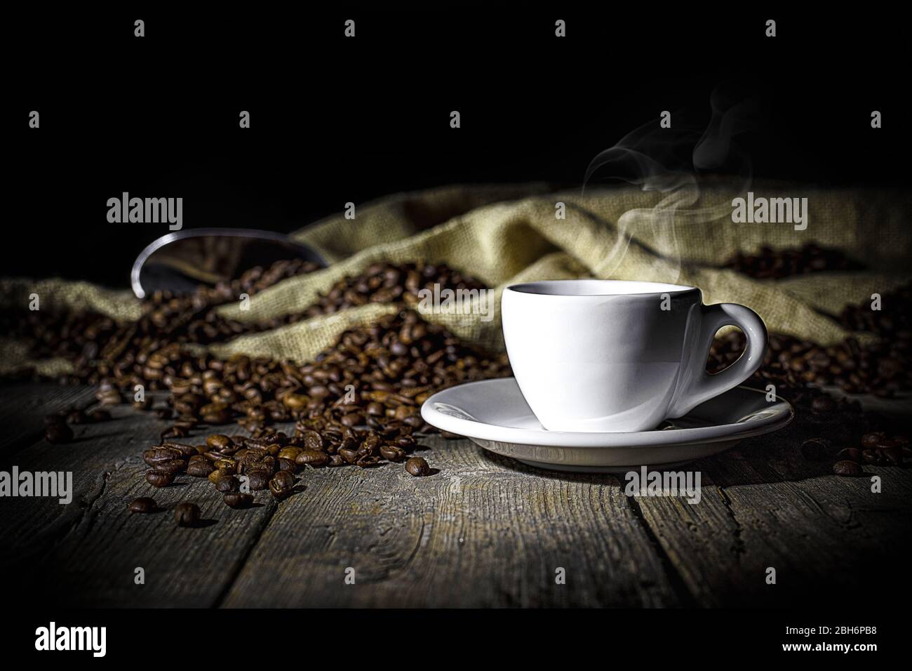 Dampfende Tasse Kaffee auf Holzhintergrund in alten Naturplanken und Sackleinen mit gerösteten Kaffeebohnen. Weiches Licht. Konzept des Getränks mit Kaffee Stockfoto