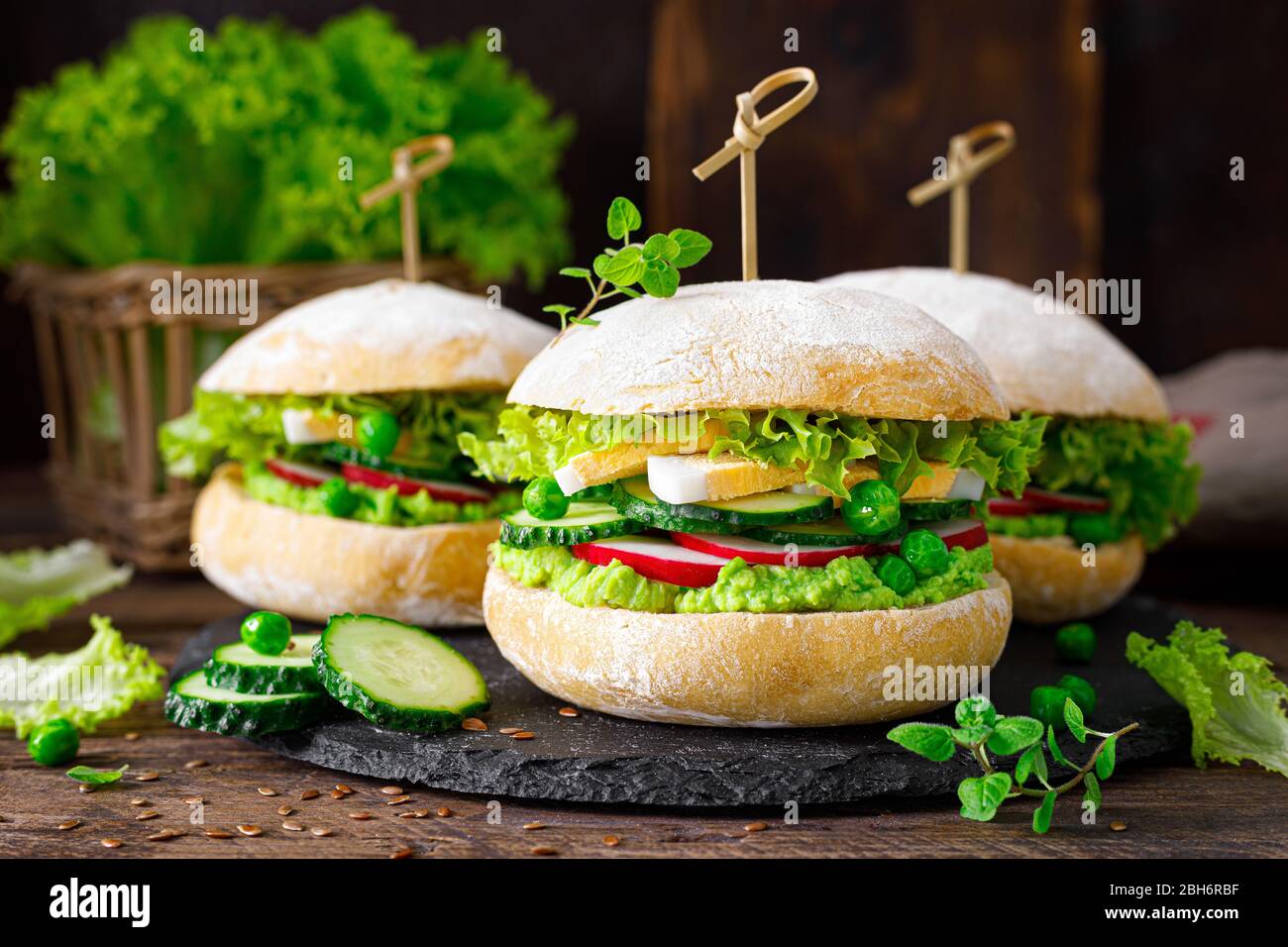 Hamburger mit hausgemachtem Ciabatta-Brötchen, gekochtem Ei, Rettich, Gurke, Salat und frischem Grünerbsen-Püree Stockfoto
