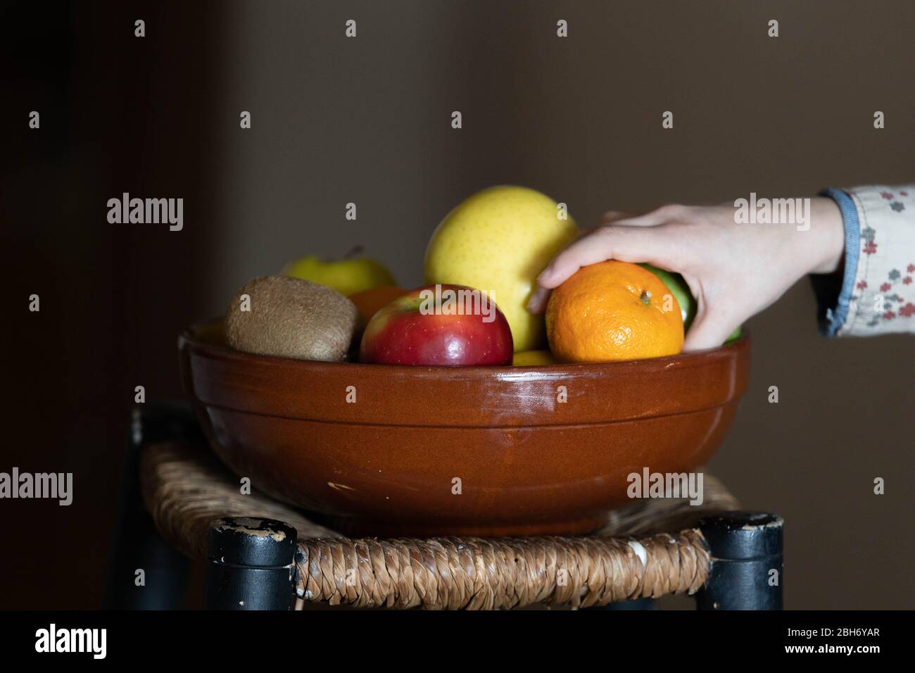 Hand Auswahl einer Mandarine aus einer Keramik-Obstschale Stockfoto