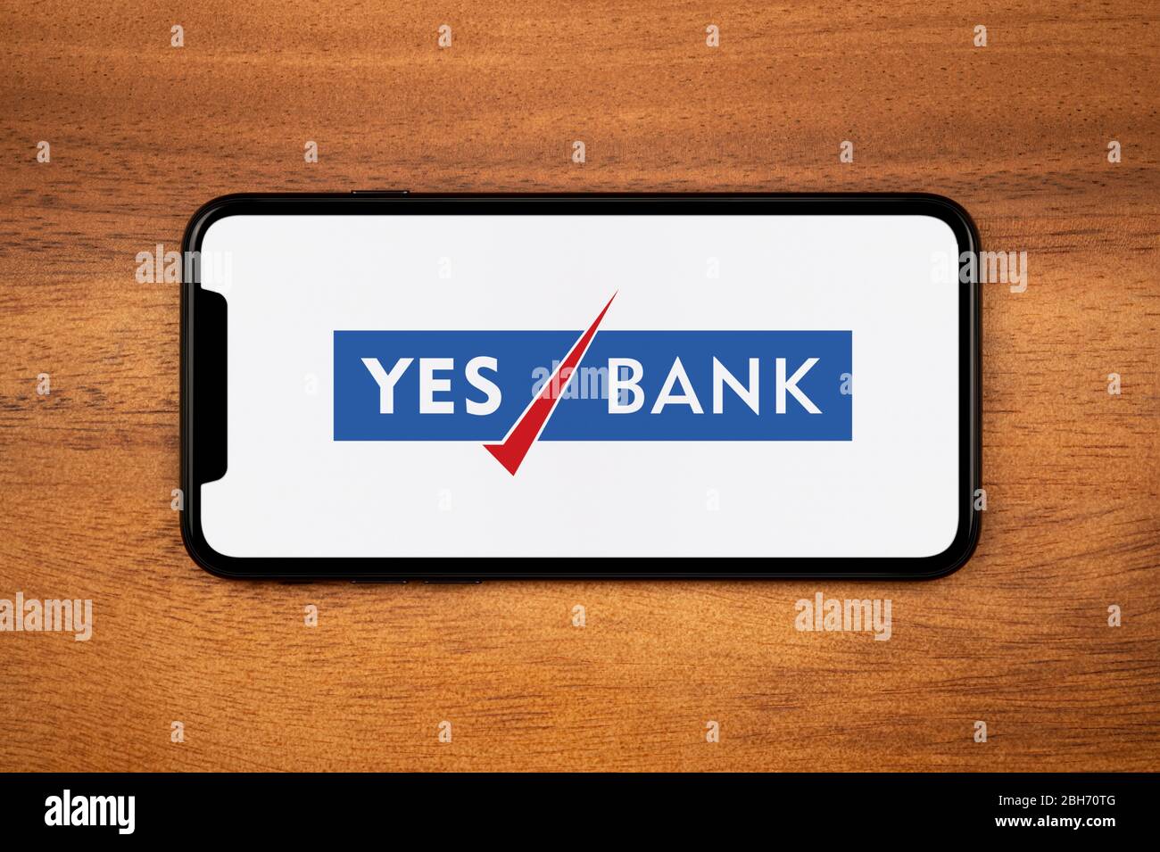 Ein Smartphone mit dem Yes Bank Logo liegt auf einem einfachen Holztisch (nur für redaktionelle Zwecke). Stockfoto