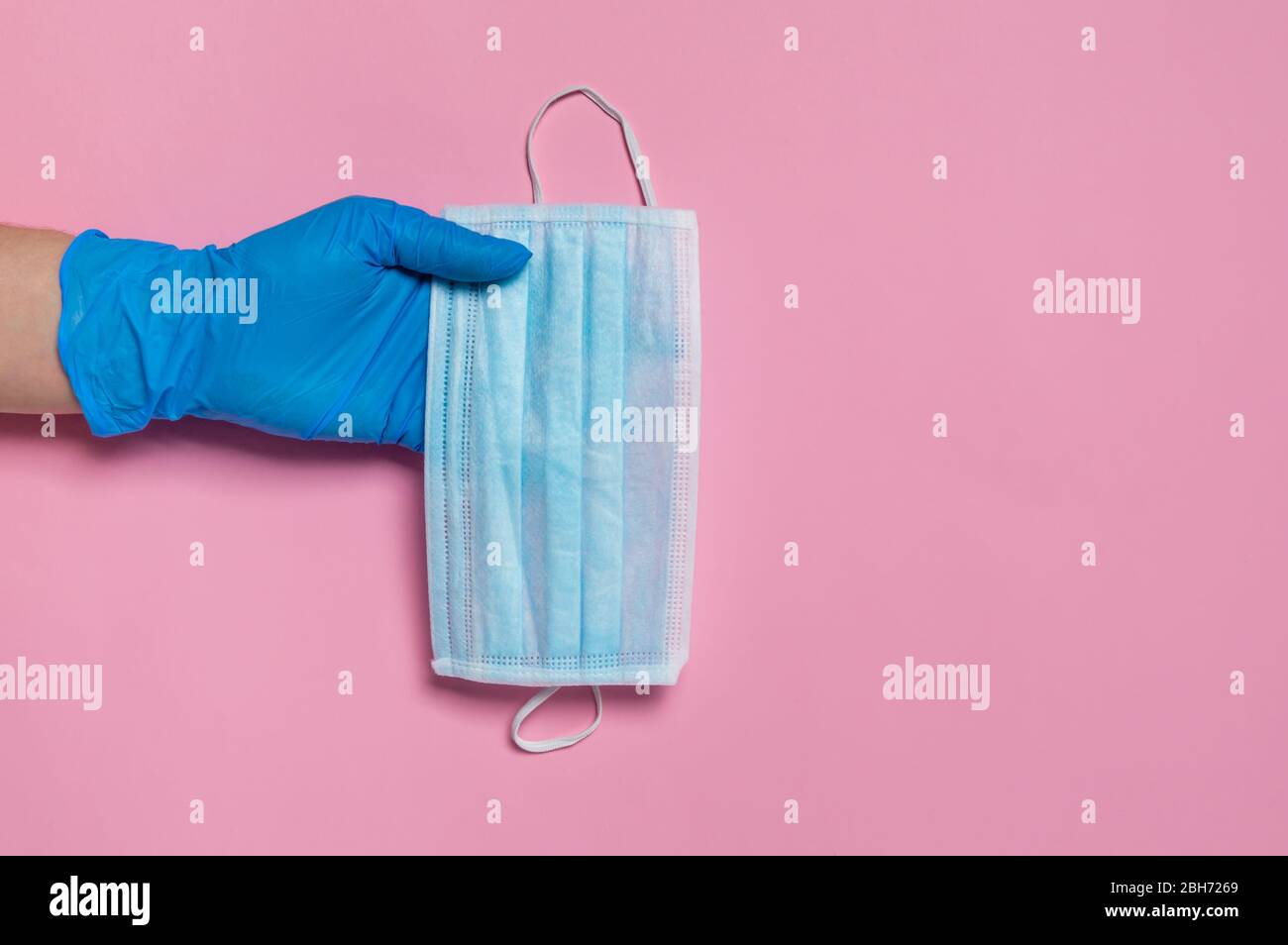 Schutz vor Coronavirus. Hand in blauen Einweg-Handschuh hält medizinische chirurgische Maske auf rosa Hintergrund. Hygienemaßnahmen zur Verhinderung der Ausbreitung von Covid-19 Stockfoto