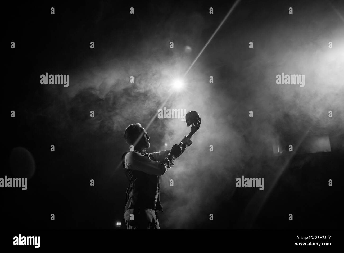 Schauspieler auf der Bühne mit Hamlet Yorik Szene mit Totenkopf, schwarz und weiß mit Scheinwerfer Stockfoto