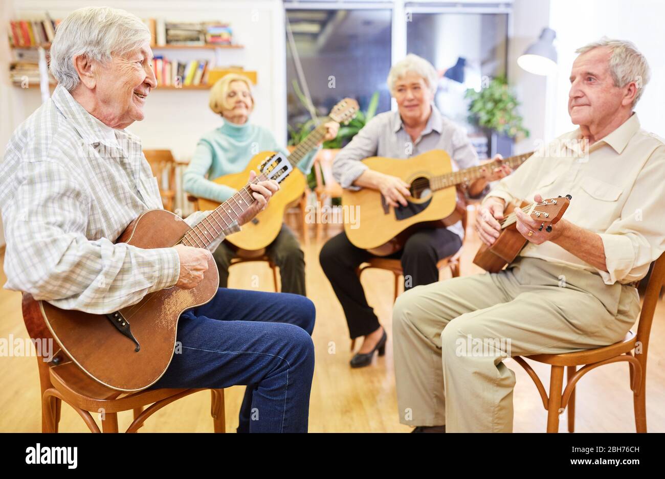 Senioren lernen gemeinsam Gitarre spielen in einem Gitarrenkurs im Altersheim Stockfoto