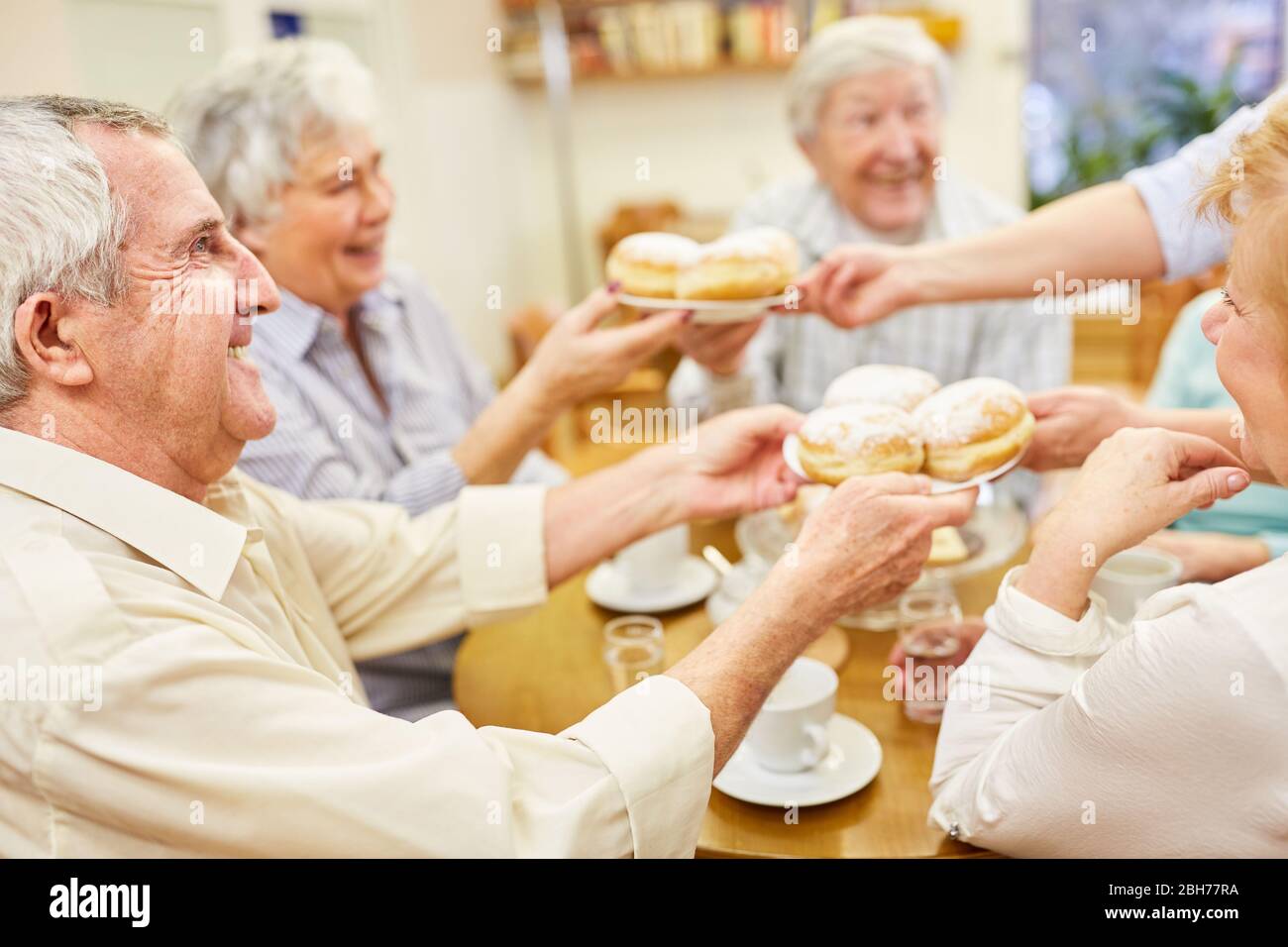 Seniorengruppe am Couchtisch mit hausgemachten Berliner Pfannkuchen Stockfoto