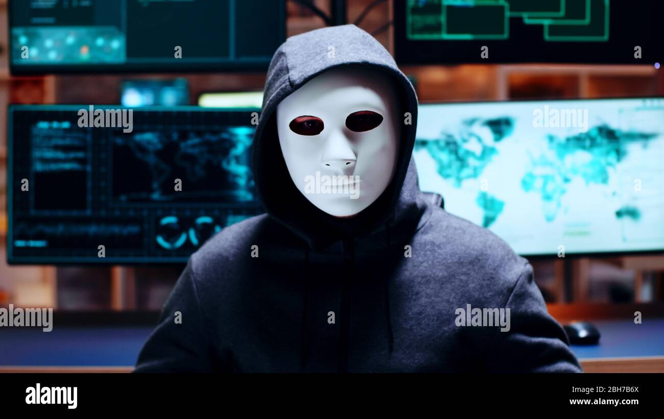 Zoom in Schuss Cyber-Kriminelle trägt eine weiße Maske Blick auf die Kamera. Stockfoto