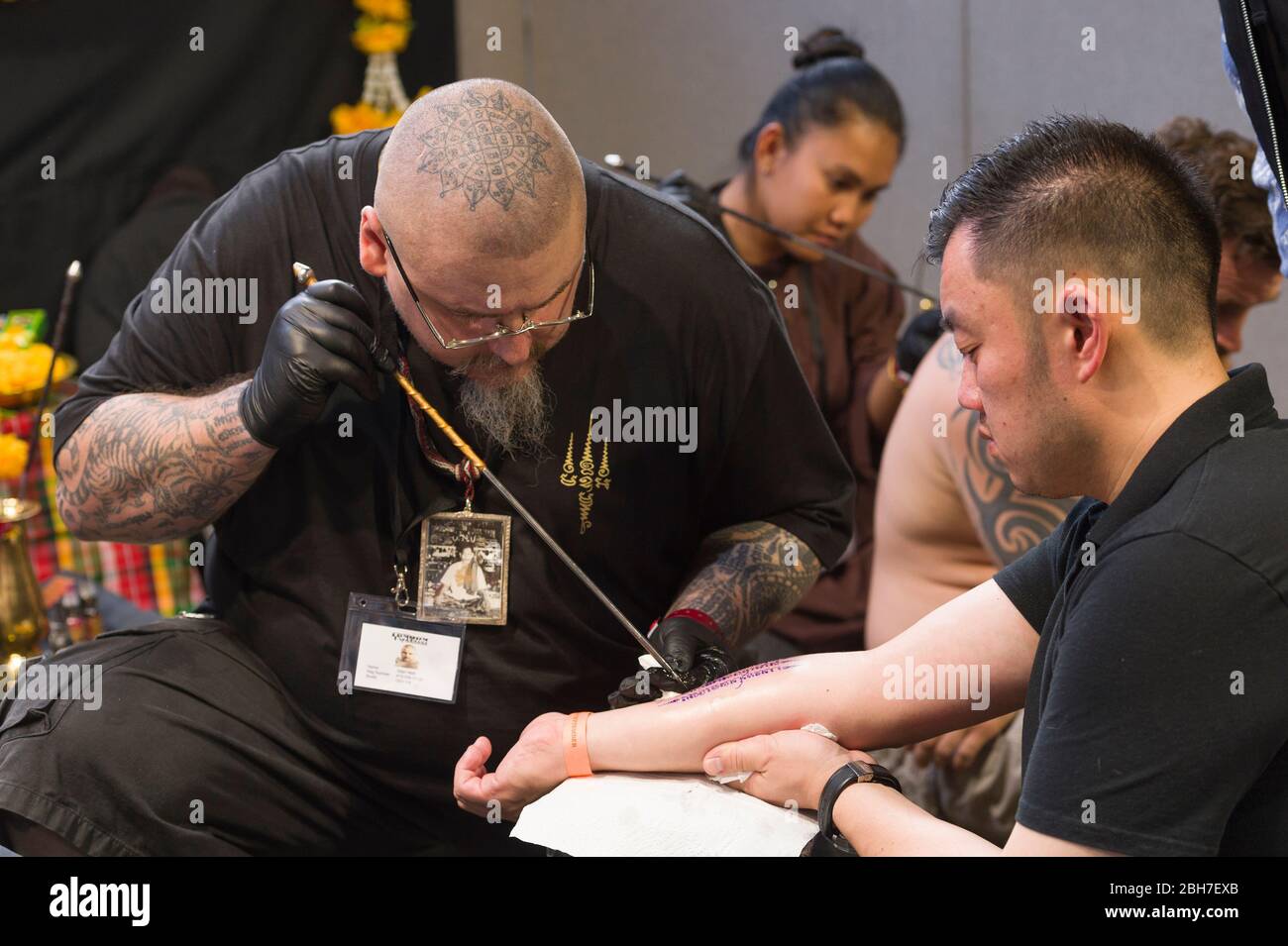 Ein Mann, der auf der 12. London Tattoo Convention 2016, Tobacco Dock, 50 Porter, ein Arm-Tattoo von einem Tätowierer mit der Metall-Tube-Tätowierungstechnik bekommt Stockfoto