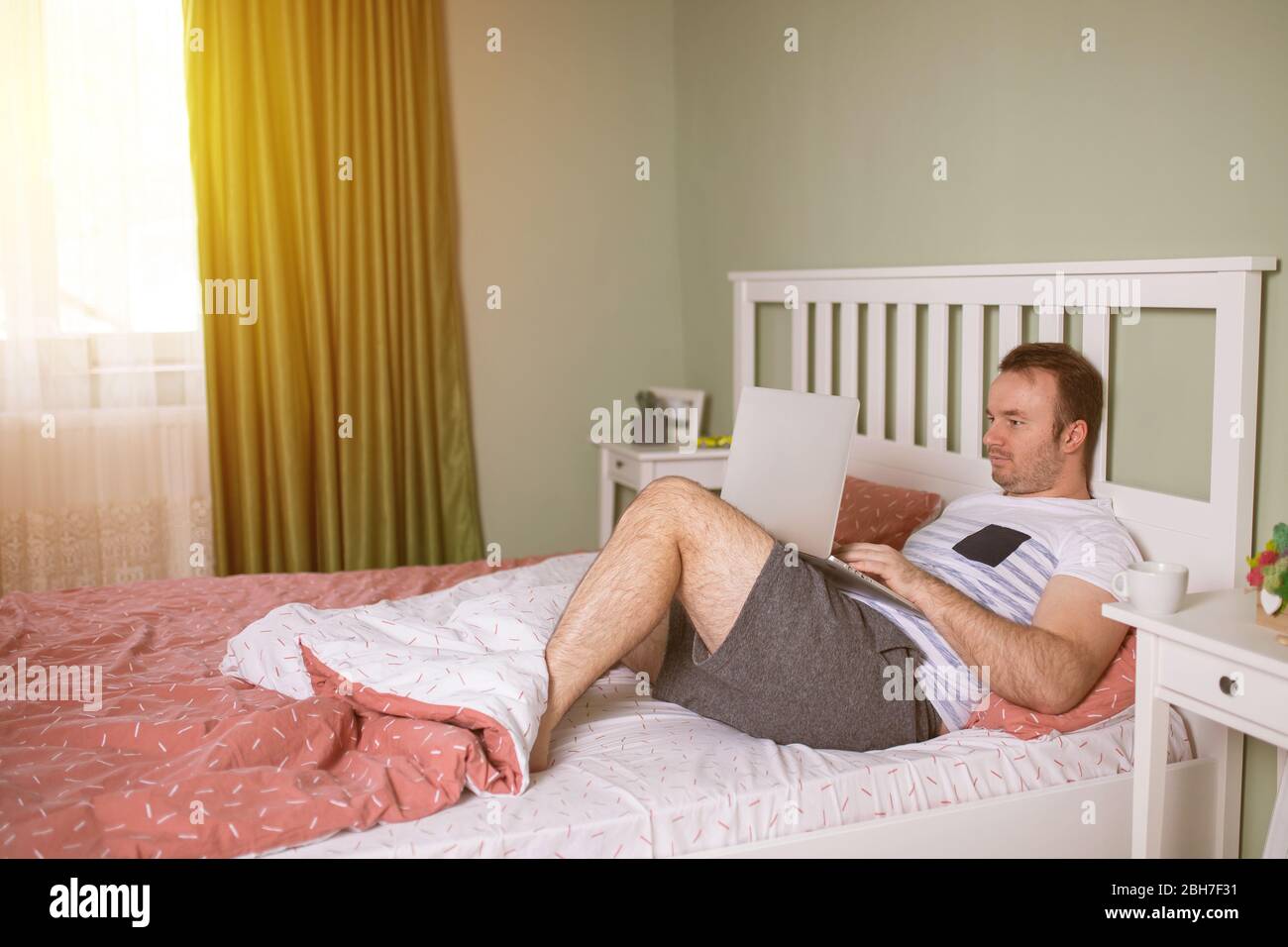 Schöner junger Mann im Pyjama mit einem Laptop während im Bett am Morgen liegen Stockfoto