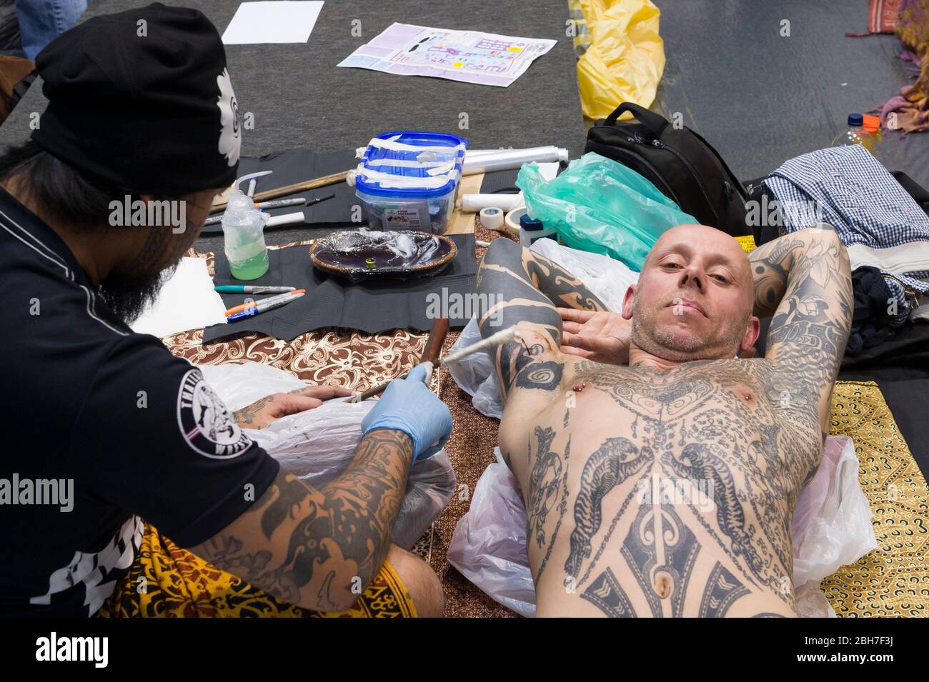 Ein Mann, der auf der 12. London Tattoo Convention 2016, Tobacco Dock, 50 Porte, ein Arm-Tattoo von einem Tätowierer mit der Rake & Stamping Stick Technik bekommt Stockfoto