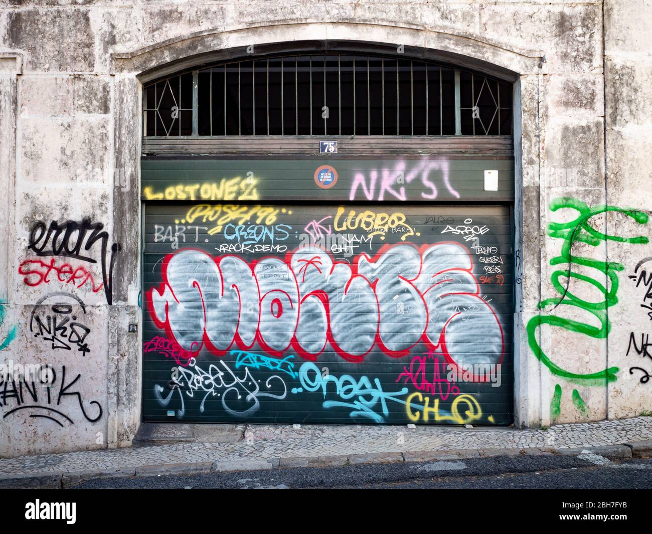 Graffiti-Tags verstellen die zerbröckelnde Pracht eines typischen Hinterstraßeneingangs in einer Garage; Lissabon, Portugal. Stockfoto