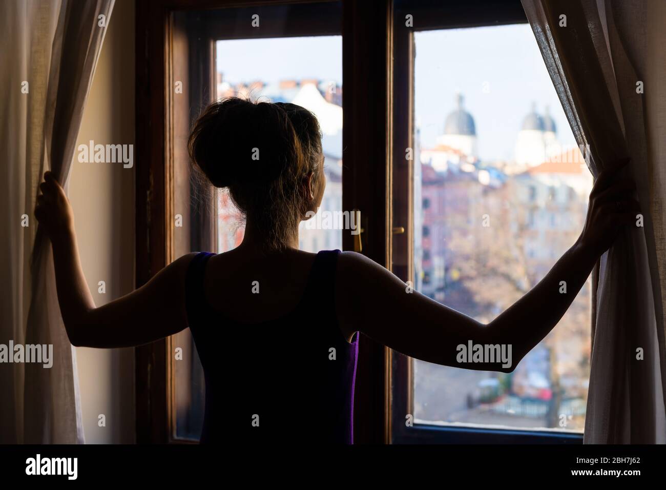 Frau zurück öffnende Vorhänge aus Wohnung Zimmer Glasfenster mit Blick auf Lviv, Ukraine alten Marktplatz in elegantem Kleid Stockfoto