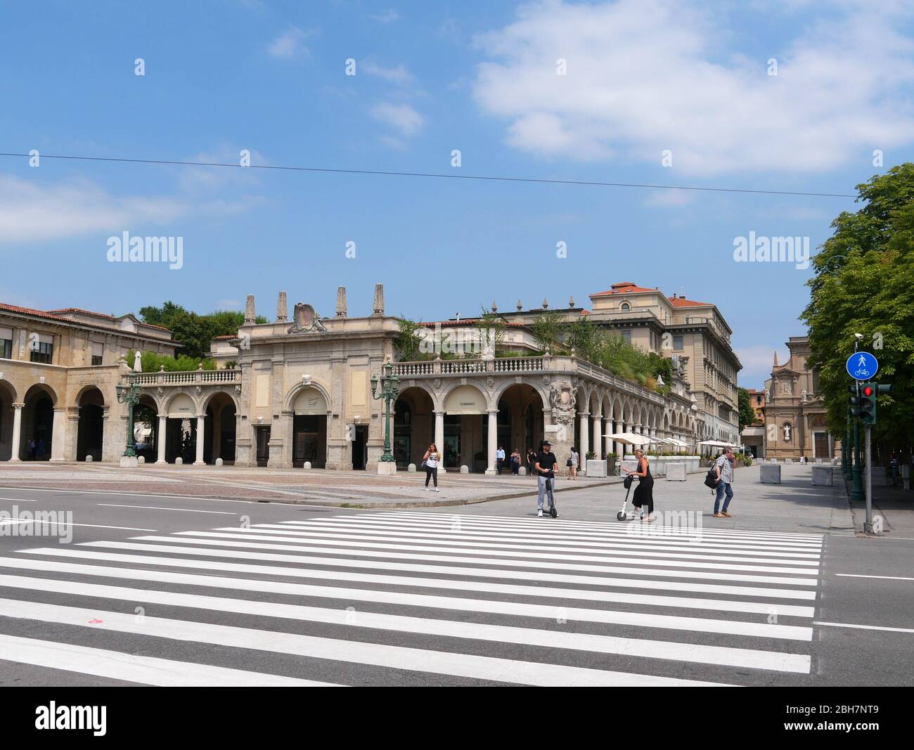 Bergamo, Italien - 06. August 2019: Personen mit Elektroscootern warten auf die Kreuzung vor Santi Bartolomeo e Stefano, eine barocke römische Katze Stockfoto