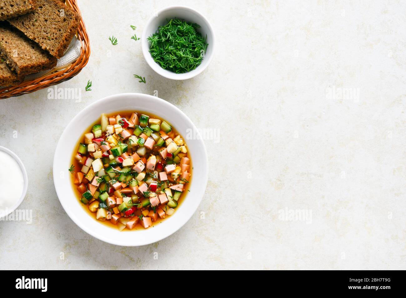Traditionelle kalte russische Suppe Okroshka mit Wurst, Gemüse und Kvass über hellsteinem Hintergrund mit freiem Textraum. Draufsicht, flacher Lay Stockfoto
