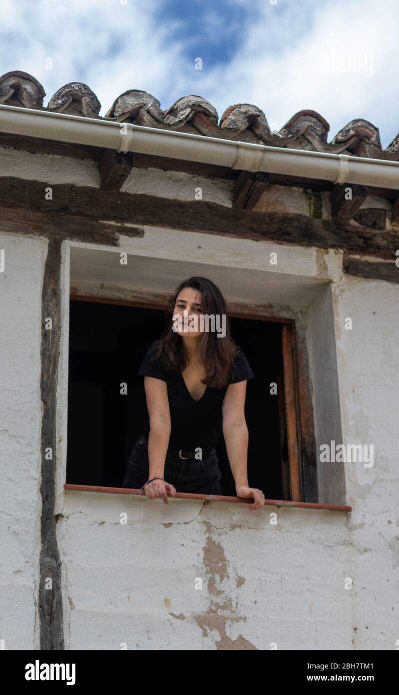 Junge Mädchen guckt aus dem Fenster ihres rustikalen Hauses. Stockfoto