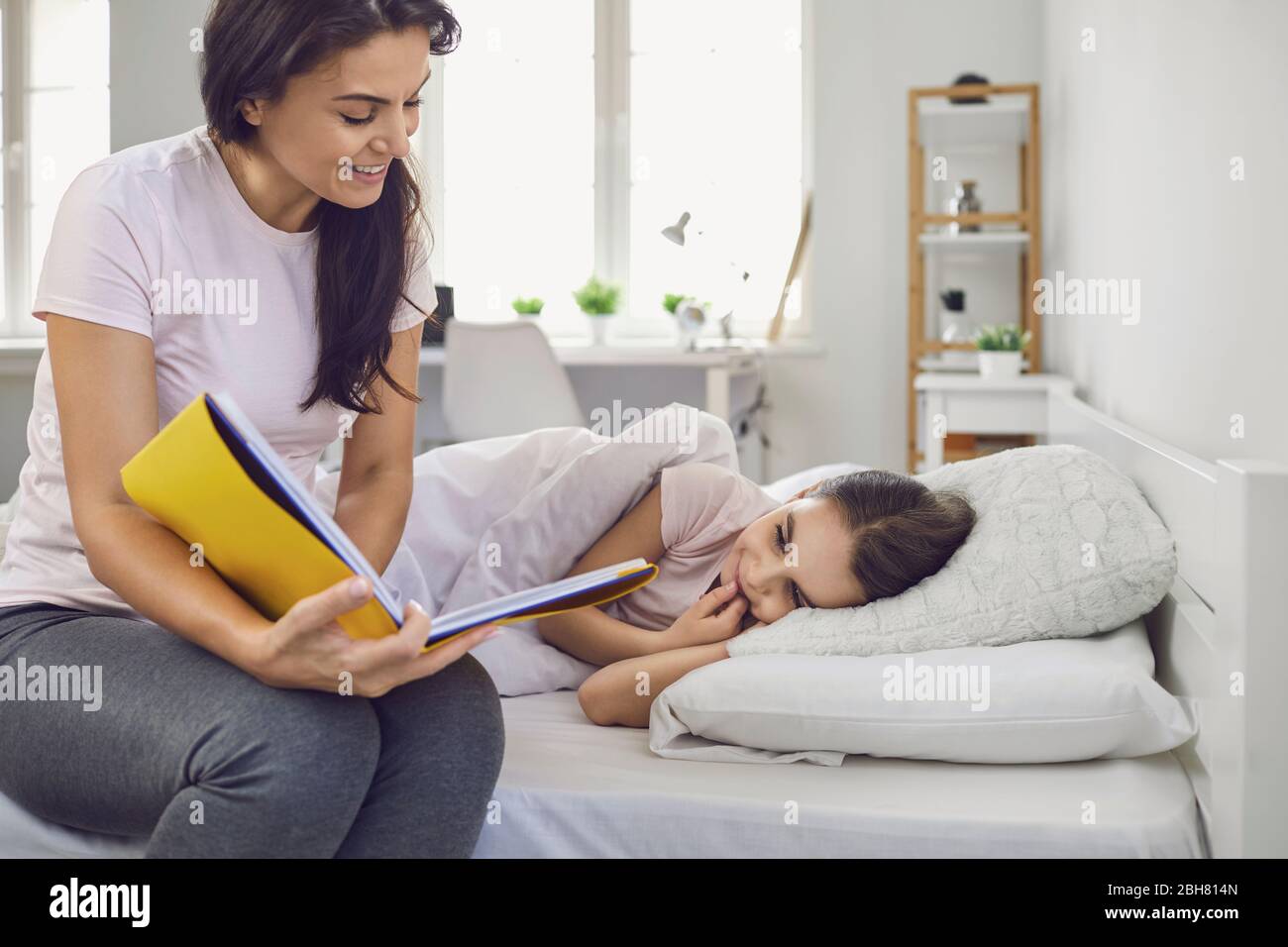 Alles Liebe zum Muttertag. Mutter und Tochter lesen ein Buch, während sie zu Hause auf dem Bett liegen. Mama liest ihrem Kind vor allem in einem Buch eine interessante Geschichte vor Stockfoto