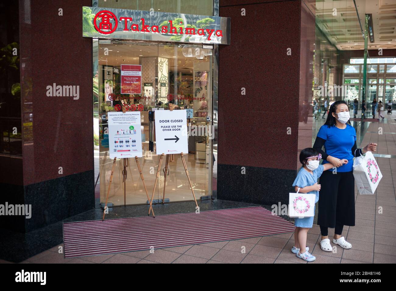 02.04.2020, Singapur, Singapur - EINE Mutter steht mit ihrem Kind vor dem Takashimaya Einkaufszentrum an der Orchard Road. Beide tragen Mundstück Stockfoto