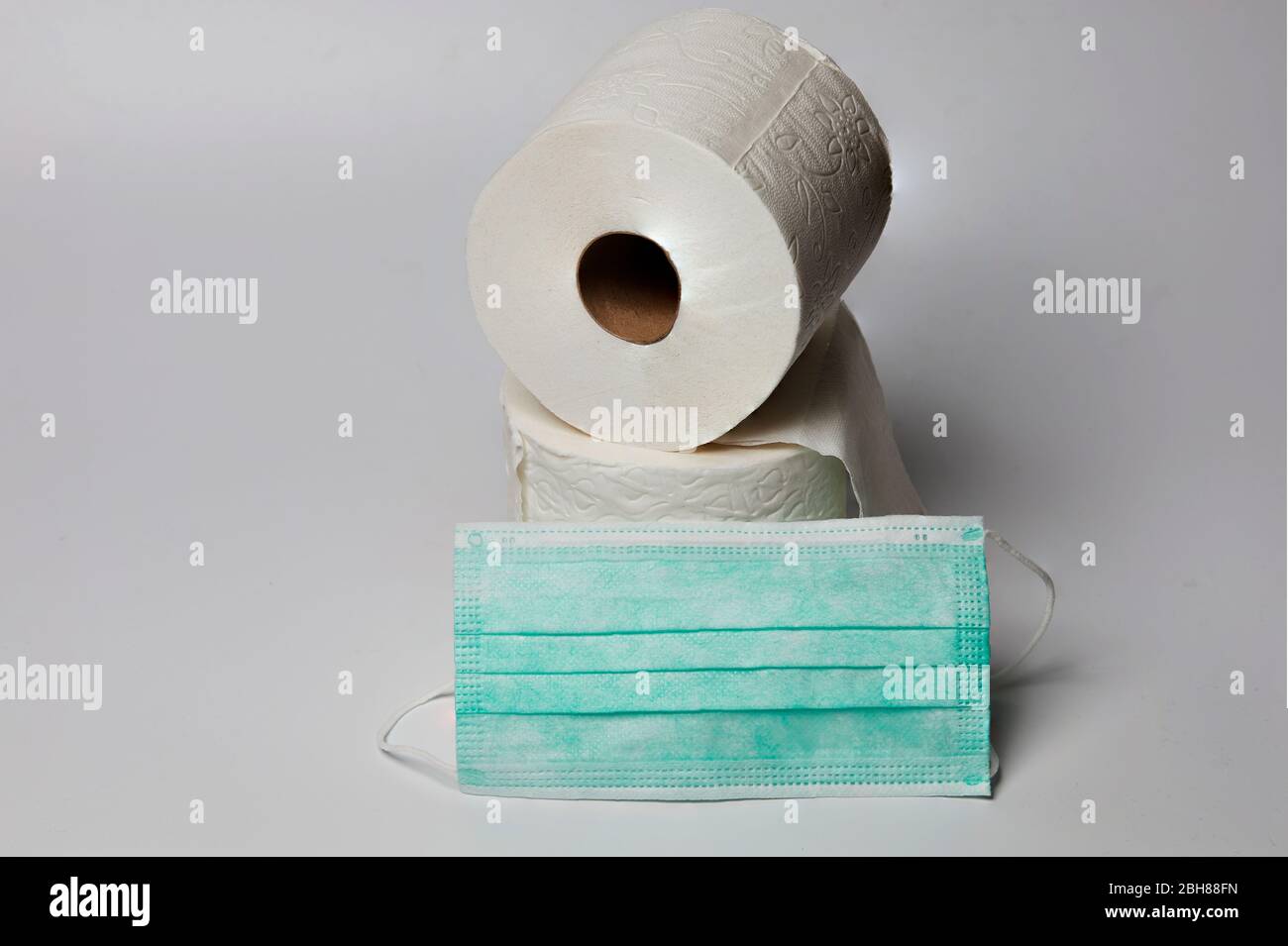 Stillleben von zwei Rollen Toilettenpapier auf weißem Hintergrund mit chirurgischer Maske Stockfoto
