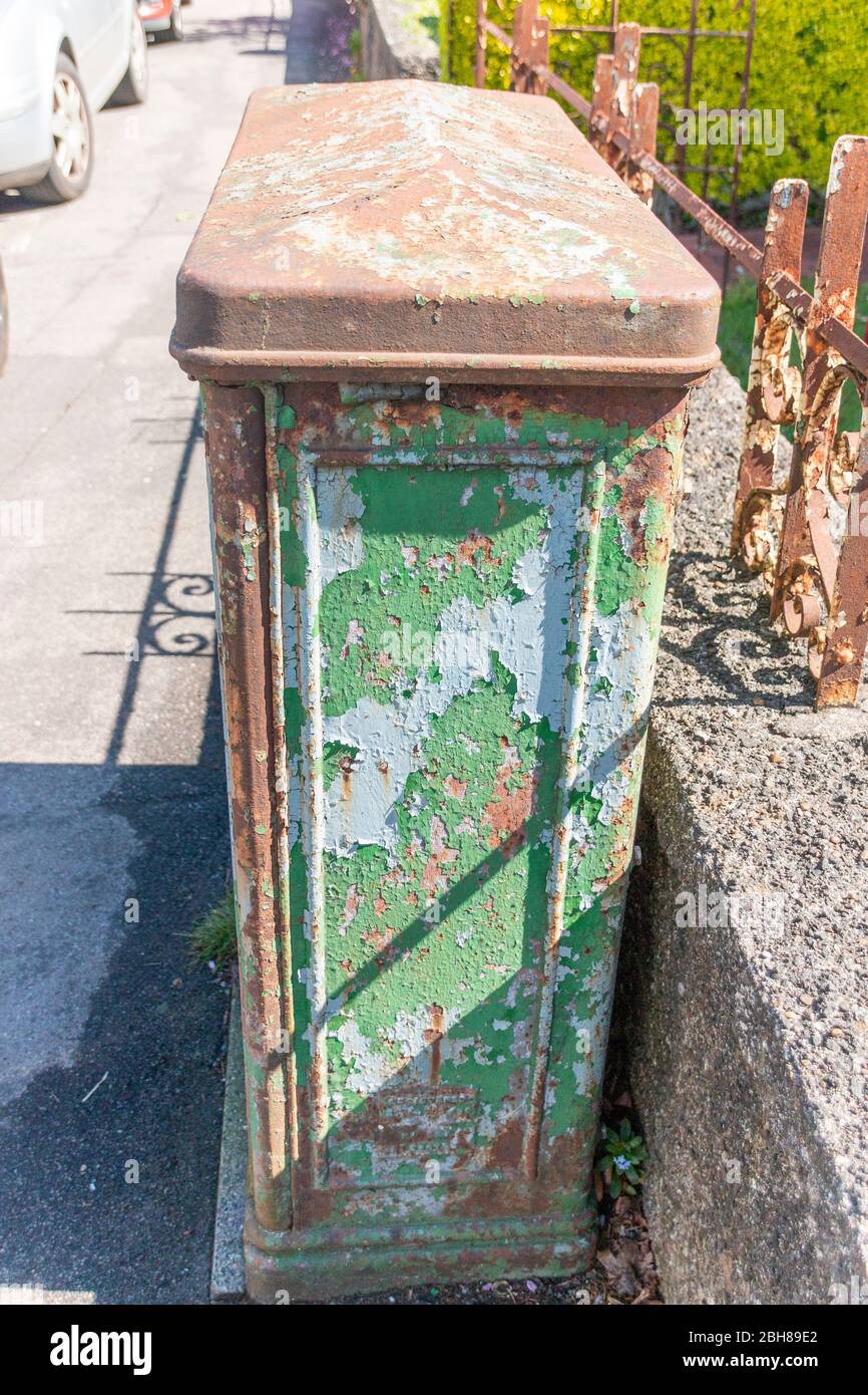 Eine Nahaufnahme eines verrosteten alten Elektrokastens auf dem Pflaster außerhalb eines Gebäudes, wo die Farbe abblättert. Stockfoto