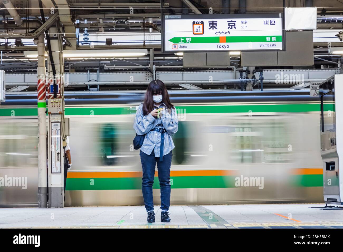 Japan, Honshu, Tokio, Tokyo Station, Yamanote Line Platform, Junge Frau mit Maske, die auf den Zug wartet Stockfoto